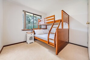 A bunk bed with a wooden frame, a small bedside table, and a window with a view of trees.