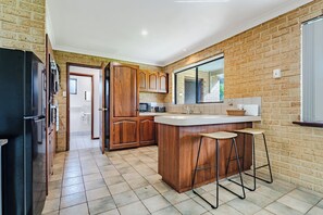 A kitchen with wooden cabinets, a black refrigerator, a white countertop, and a window.