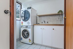 A laundry room with a stacked washer and dryer, a sink with a wooden countertop, and a tiled backsplash.