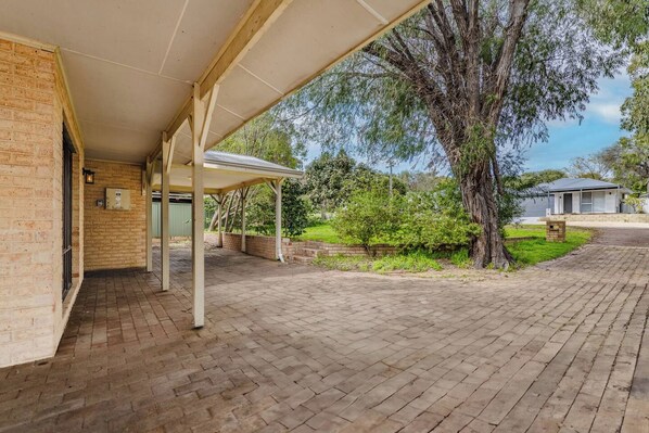 A covered outdoor area with a brick wall, a tree, and a paved walkway.