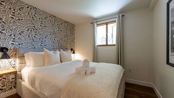 A neatly made bed with white linens and a rolled towel, a bedside lamp, and a patterned wall.