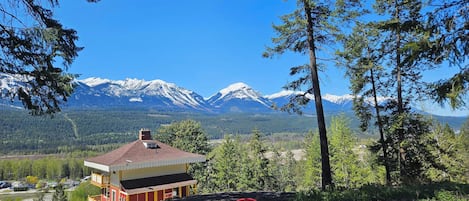 Eine Hütte mit rotem Dach und gelben Wänden, zwei rote Adirondack-Stühle und Blick auf schneebedeckte Berge.
