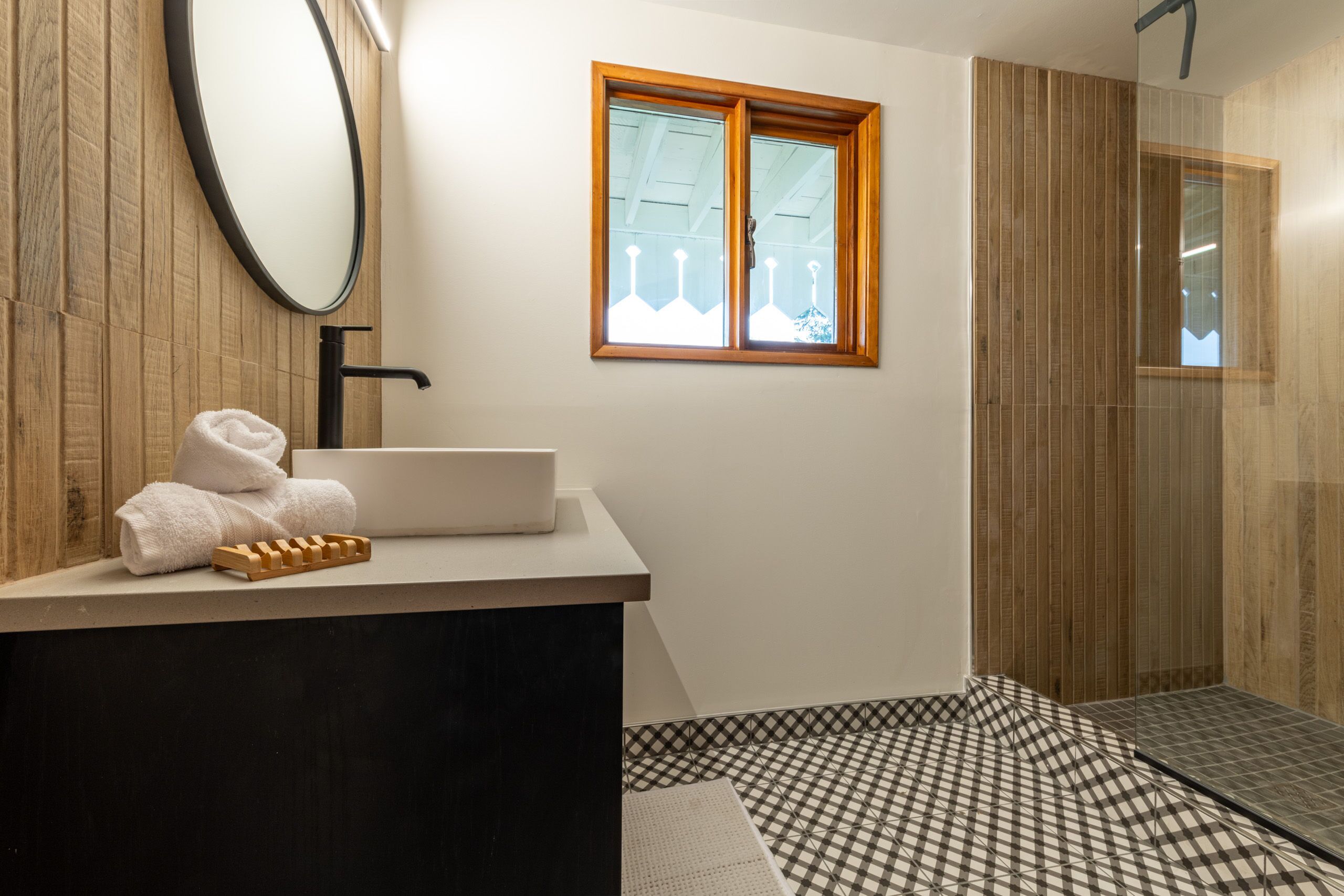 A bathroom with a wooden vanity, a mirror, a window, and a checkered floor.