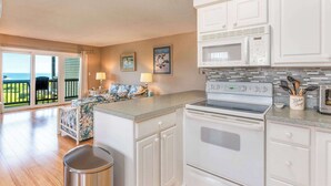 A kitchen with white cabinets, a microwave, a stove, and a trash can. There is a balcony with a view. - In Duck with Community Pool & Beach Access (Duck)