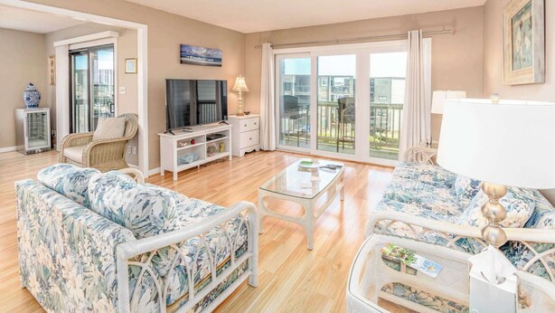 A living room with a sofa, a coffee table, a TV, and a balcony with a view. - In Duck with Community Pool & Beach Access (Duck)