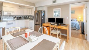 A compact kitchen with white cabinets, a refrigerator, and a dining area with a table and chairs. - In Duck with Community Pool & Beach Access (Duck)