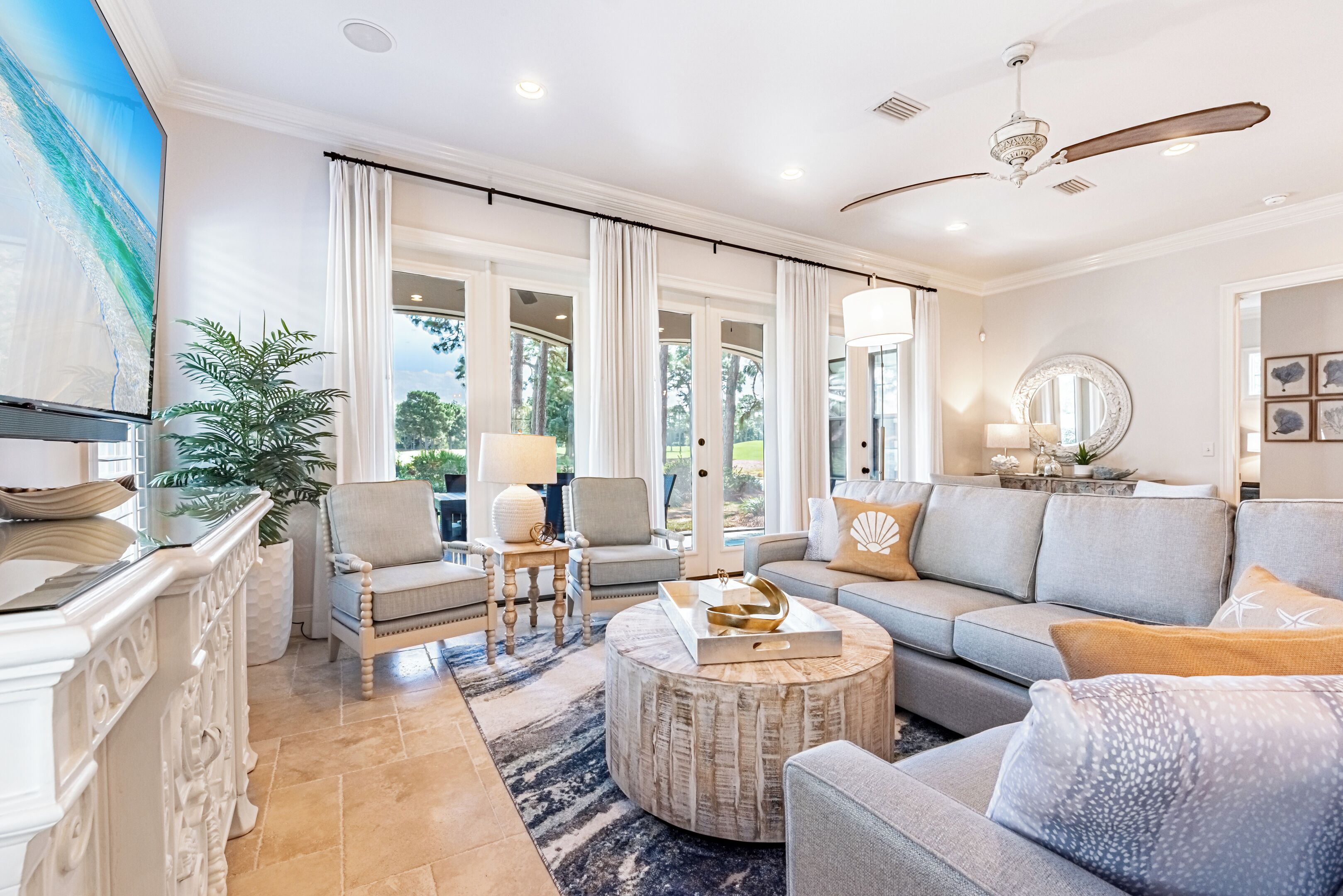 A spacious living room with a large window, a ceiling fan, and a round coffee table.
