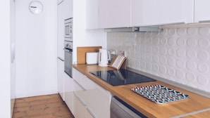 A modern kitchen with white cabinets, a wooden countertop, a built-in oven, and a patterned backsplash. - Chic & Luxurious 2-BR Escape Designed for Elegance (Gibraltar)