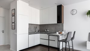 A modern kitchen with white cabinets, a grey countertop, a black range hood, and a small bar area with two stools. - Stylish studio near the National Library (Minsk)