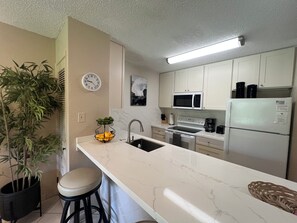 A modern kitchen with white cabinets, a microwave, a refrigerator, a sink, and a bar stool.