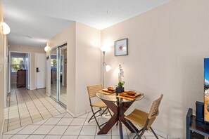Un comedor con una mesa de vidrio, sillas de mimbre y una lámpara fijada a la pared.