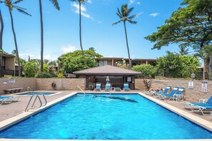 A swimming pool with blue water, surrounded by lounge chairs and a covered area.