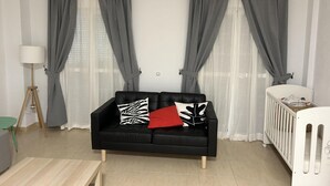 A modern living room with a black leather sofa, a small round table, and a white crib.