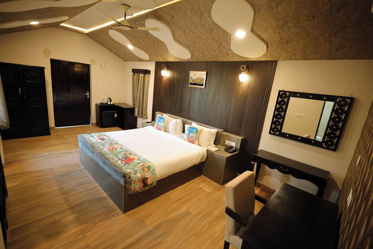 A modern hotel room with a large bed, a desk, a chair, and a mirror.