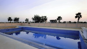 Une piscine rectangulaire à l’eau d’un bleu limpide, entourée d’une basse clôture blanche et de palmiers.