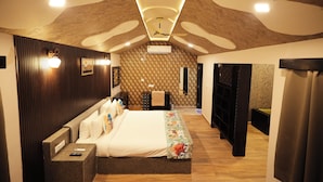 Une chambre avec un grand lit, une table de chevet avec une télécommande, un climatiseur fixé au mur et un mur décoré d’un motif.