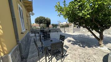 An outdoor patio with a table and chairs, a tree, and a view of the sea.