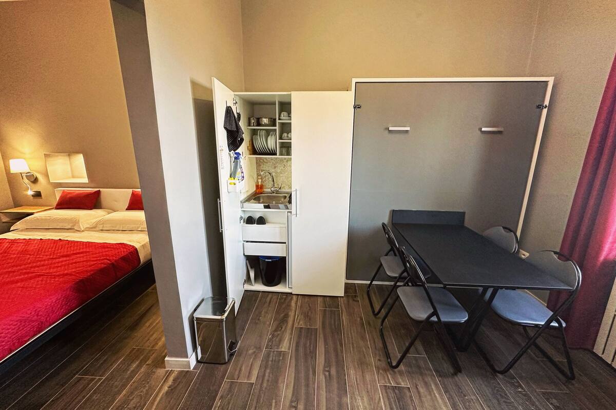 A compact hotel room with a bed, a small kitchenette, a foldable table with chairs, and a wardrobe.
