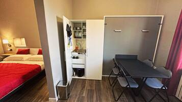 Una camera d'albergo compatta con un letto, angolo cottura, un tavolino pieghevole con sedie e un armadio.