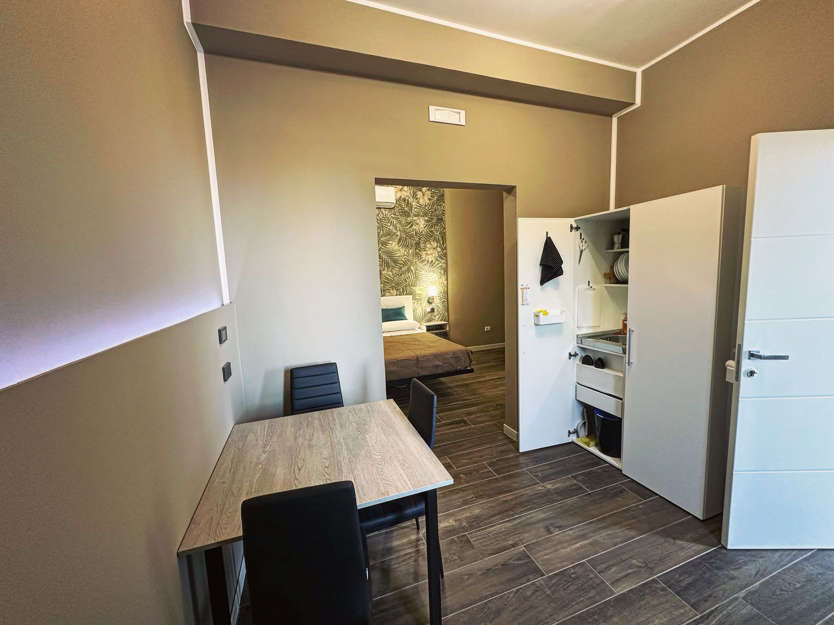 Een compacte kamer met een eettafel, stoelen, een bed, een kleine kitchenette en een kledingkast.