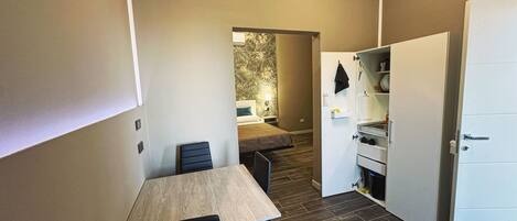 Een compacte kamer met een eettafel, stoelen, een bed, een kleine kitchenette en een kledingkast.