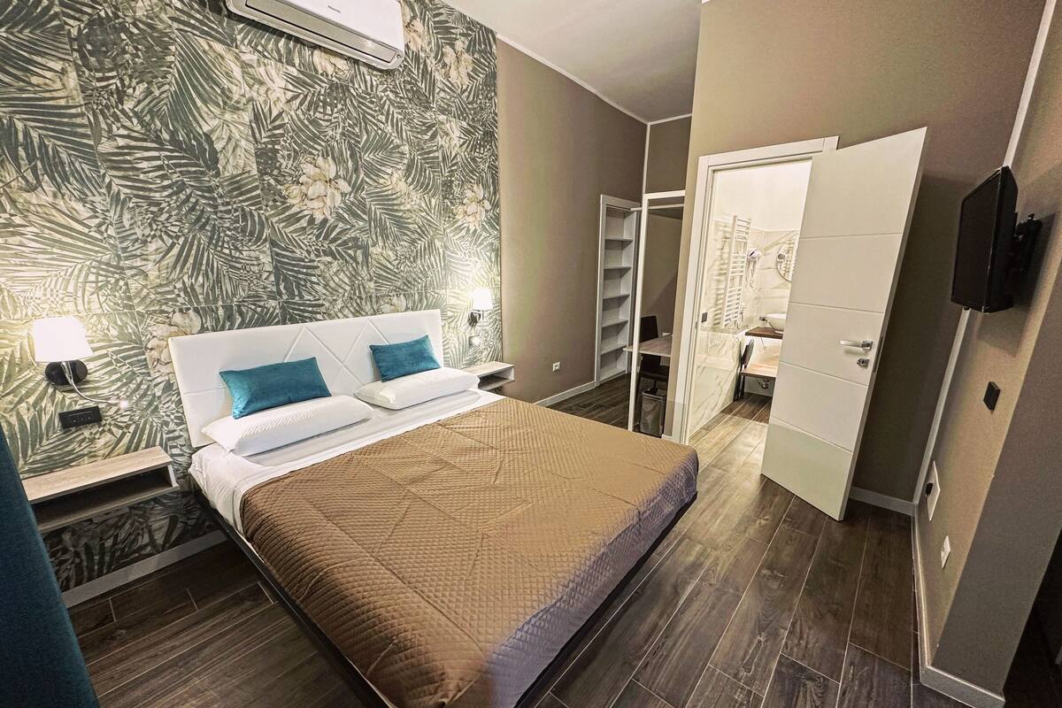 A modern bedroom with a large bed, a nightstand, a wall-mounted air conditioner, and a wardrobe.