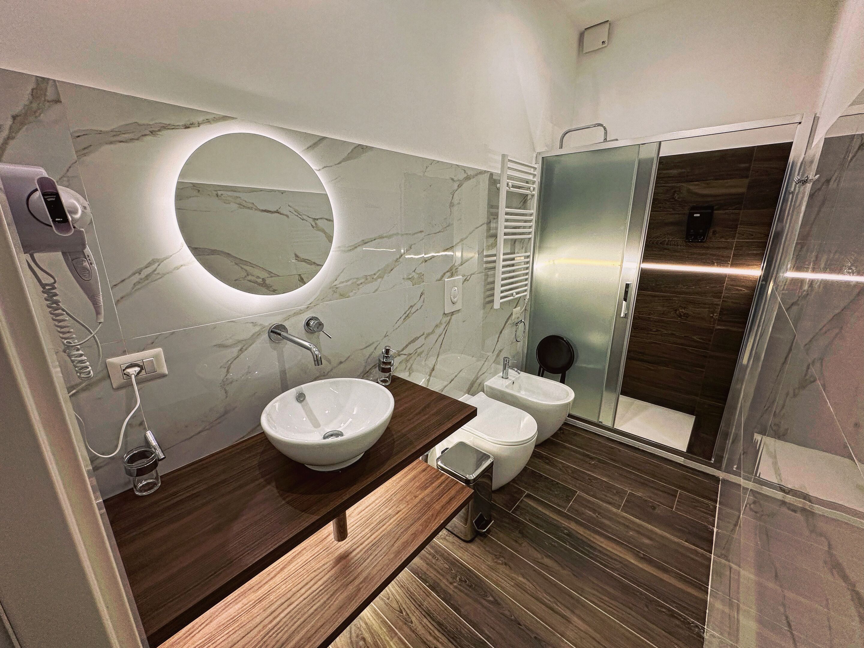 A modern bathroom with a marble vanity, a round mirror, a toilet, and a shower area.