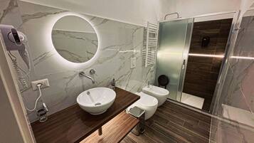 A modern bathroom with a marble vanity, a round mirror, a toilet, and a shower area.