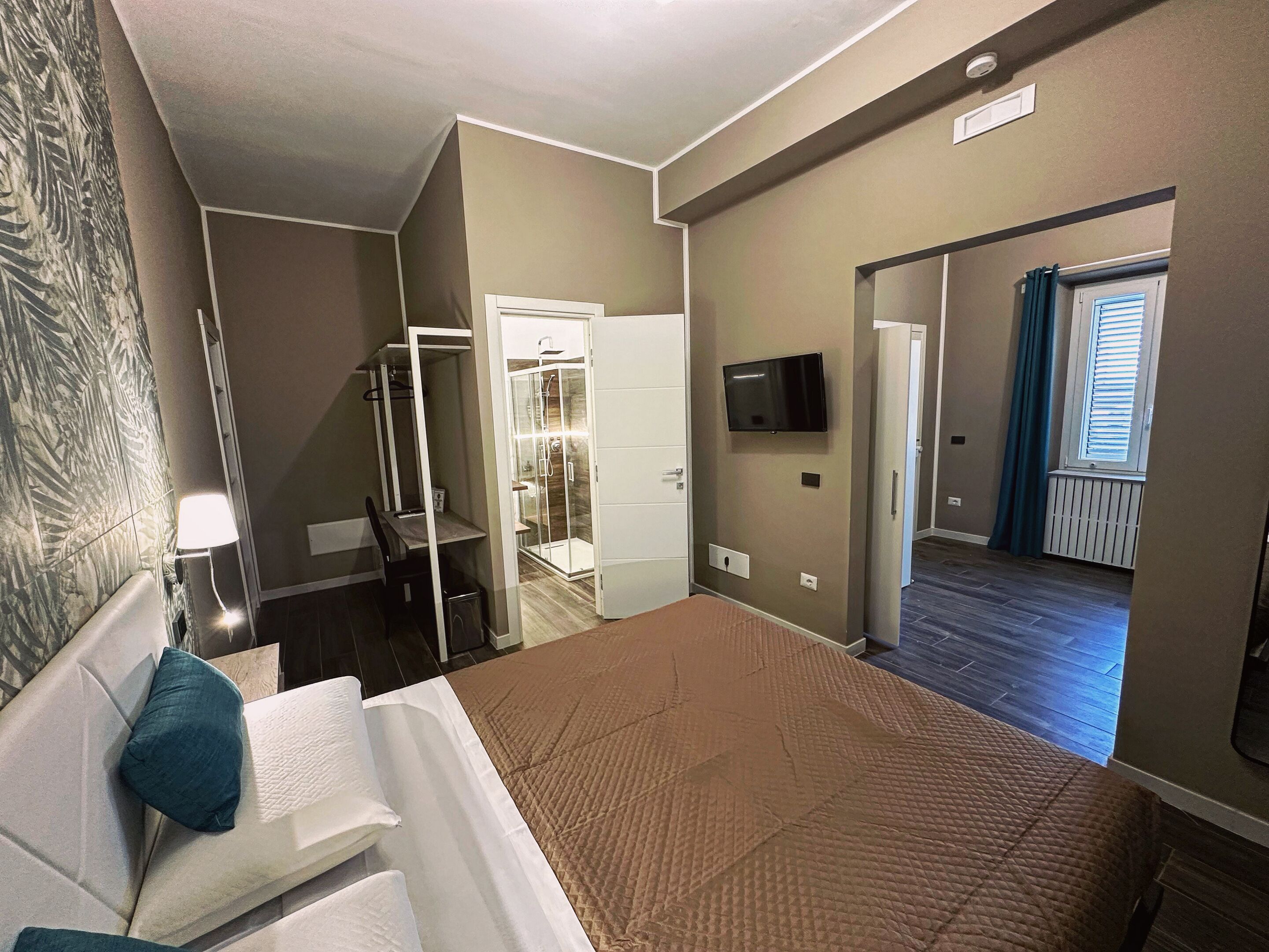 A bedroom with a bed, a walk-in closet, a shower room, a TV mounted on the wall, and a window with curtains.