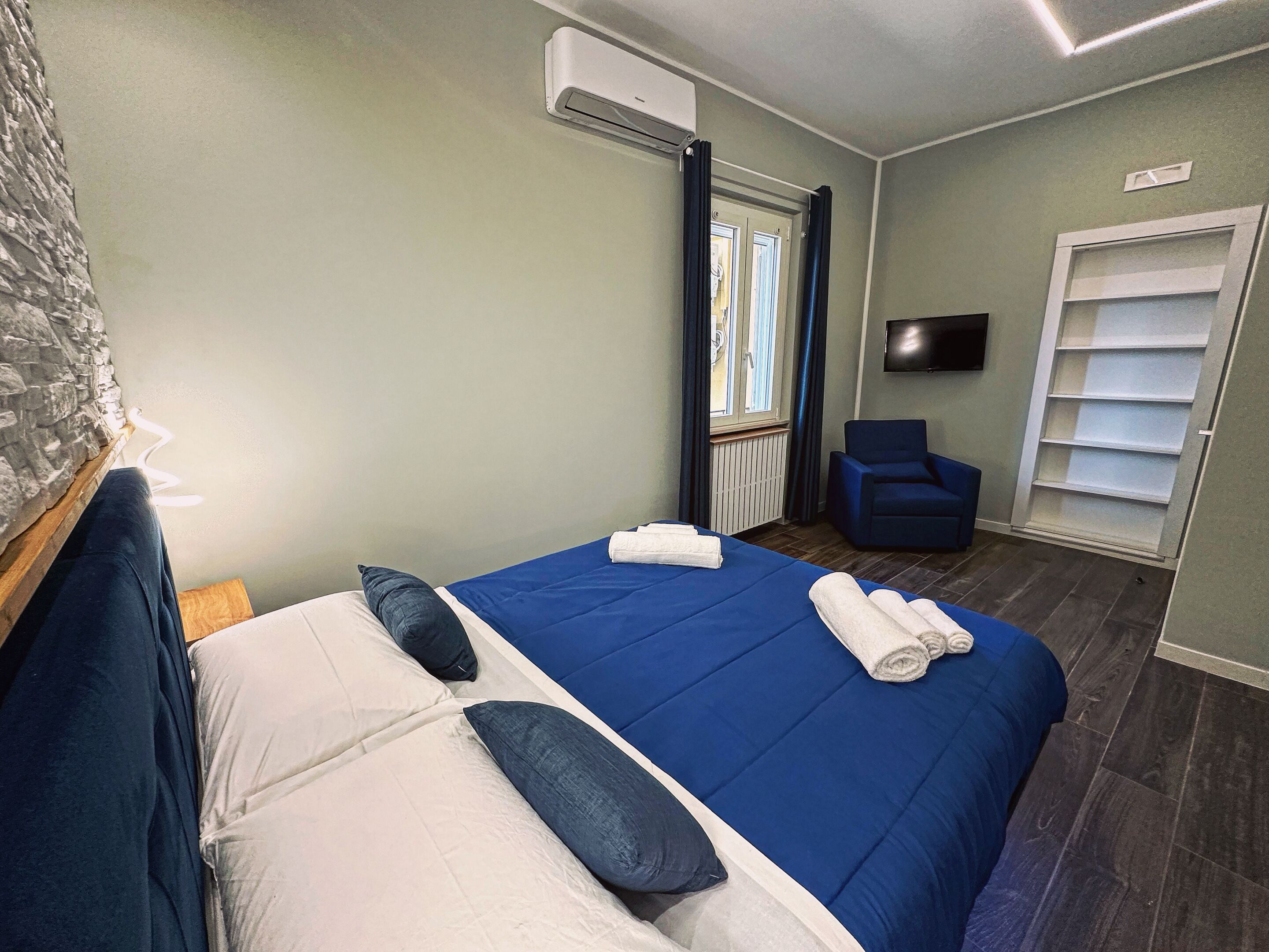 Une chambre d’hôtel avec un lit, une chaise, une télévision et une fenêtre avec des rideaux.
