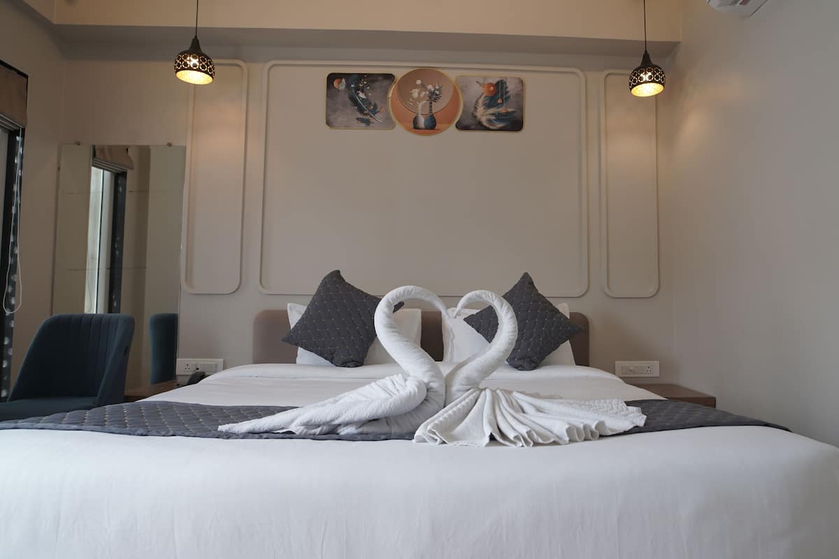Habitación de hotel con una cama bien tendida, dos lámparas fijadas a la pared y tres cuadros colgados sobre la cama.