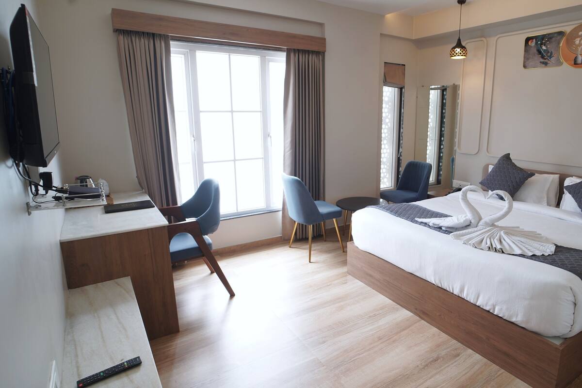 Una habitación de hotel con una cama grande, un escritorio con computadora, dos sillas, un televisor y obras de arte en la pared.