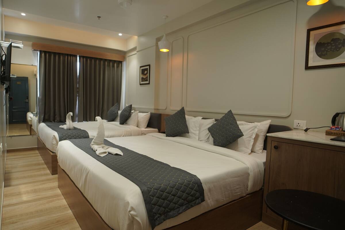 Habitación de hotel con dos camas, piso de madera, escritorio con hervidor y un cuadro en la pared.