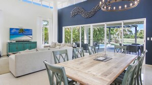 A spacious living room with a wooden dining table, green chairs, a sofa, and a television on a cabinet. - Luxury Golf Villa in Bavaro Cocotal Palma Real Pool Jacuzzi Staff (Punta Cana)