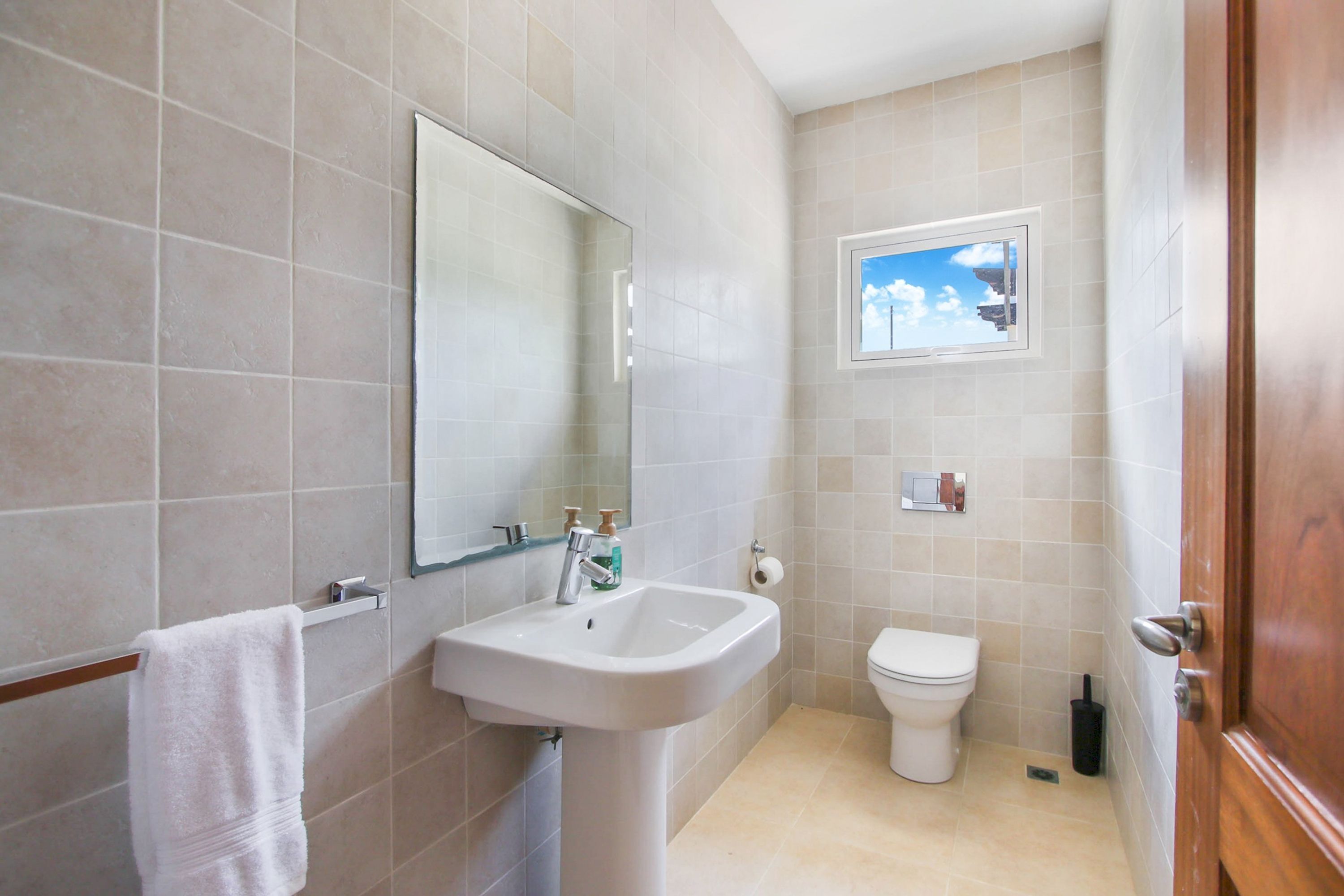 Une salle de bain équipée d’un lavabo, d’un miroir, de toilettes et d’une fenêtre donnant sur le ciel.