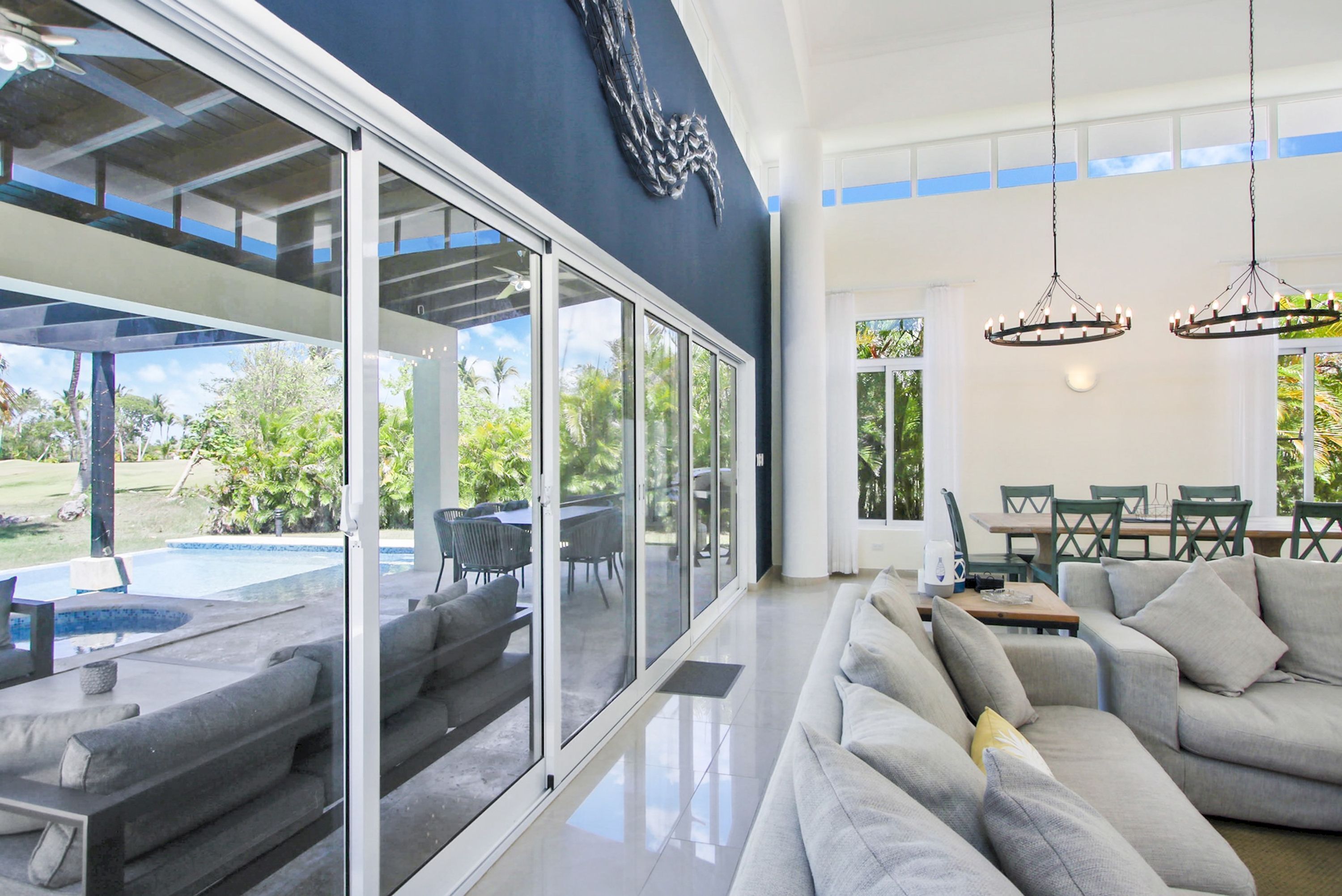 Ein modernes Wohnzimmer mit einer großen Couch, einem Essbereich mit grünen Stühlen und einer Glaswand mit Blick auf Pool und Garten.