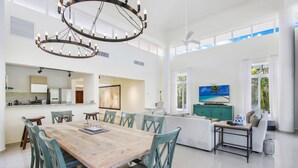 A spacious living area with a large wooden dining table and teal chairs, a kitchen with modern appliances, and a large window offering a view of the outdoors. - Luxury Golf Villa in Bavaro Cocotal Palma Real Pool Jacuzzi Staff (Punta Cana)