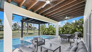 A covered outdoor area with a pool, seating, and a view of a tropical landscape. - Luxury Golf Villa in Bavaro Cocotal Palma Real Pool Jacuzzi Staff (Punta Cana)