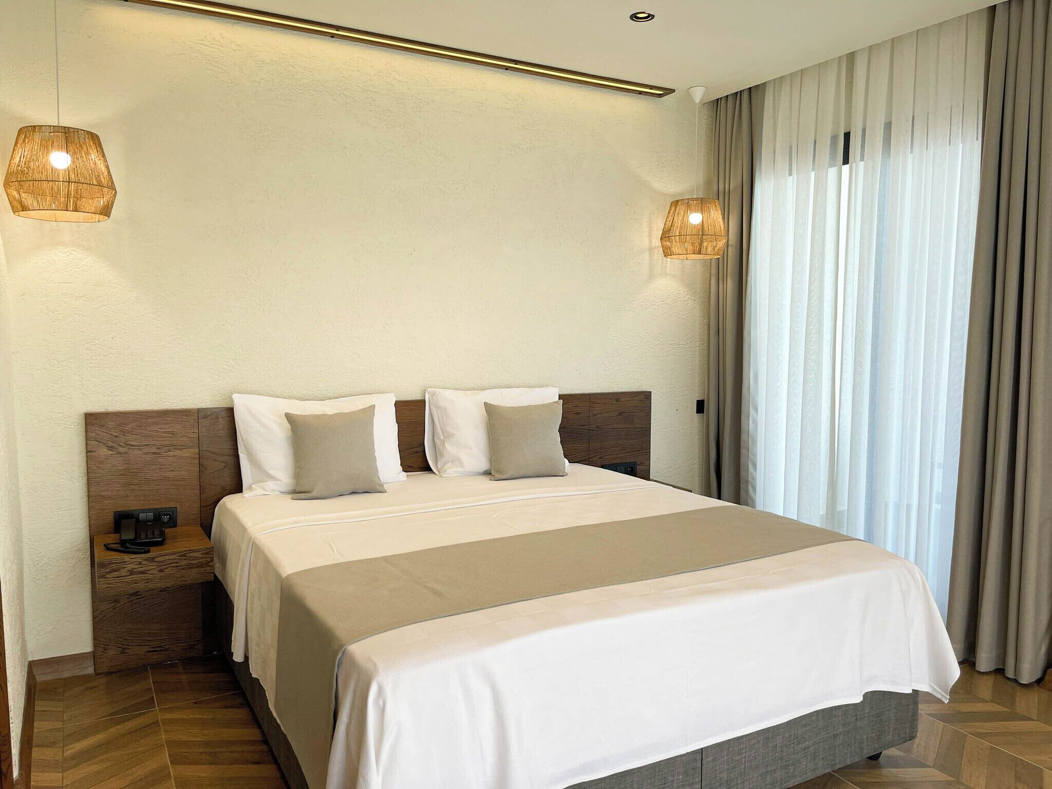 A hotel room with a large bed, two bedside tables, a nightstand, and a window with curtains.