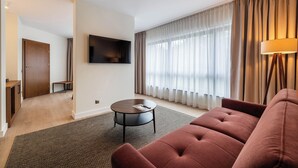 Un saló modern amb un sofà, una taula de centre rodona, un televisor de pantalla plana muntat a la paret i una finestra gran amb cortines.