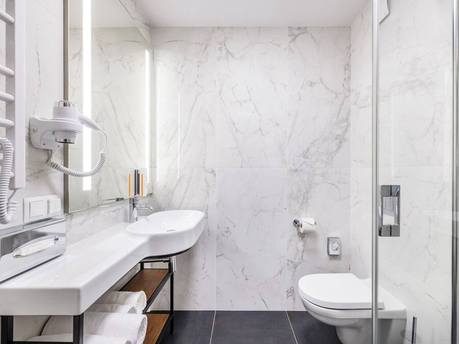 Ein modernes Badezimmer mit weißer Marmorwand, einer Duschkabine aus Glas, einem weißen Waschbecken und einer Toilette.