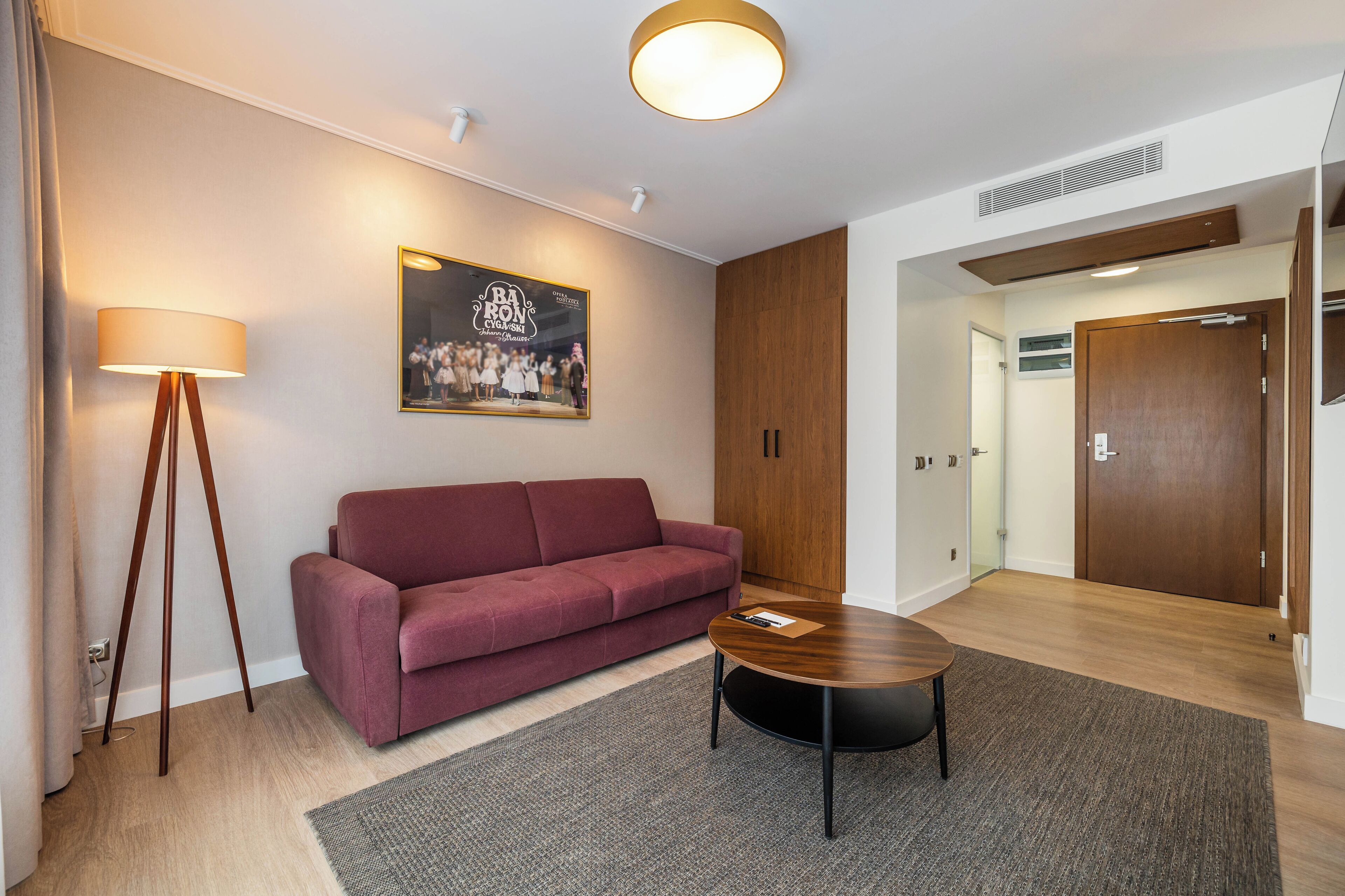 A modern room with a red sofa, a round wooden coffee table, a standing floor lamp, and a framed picture on the wall.