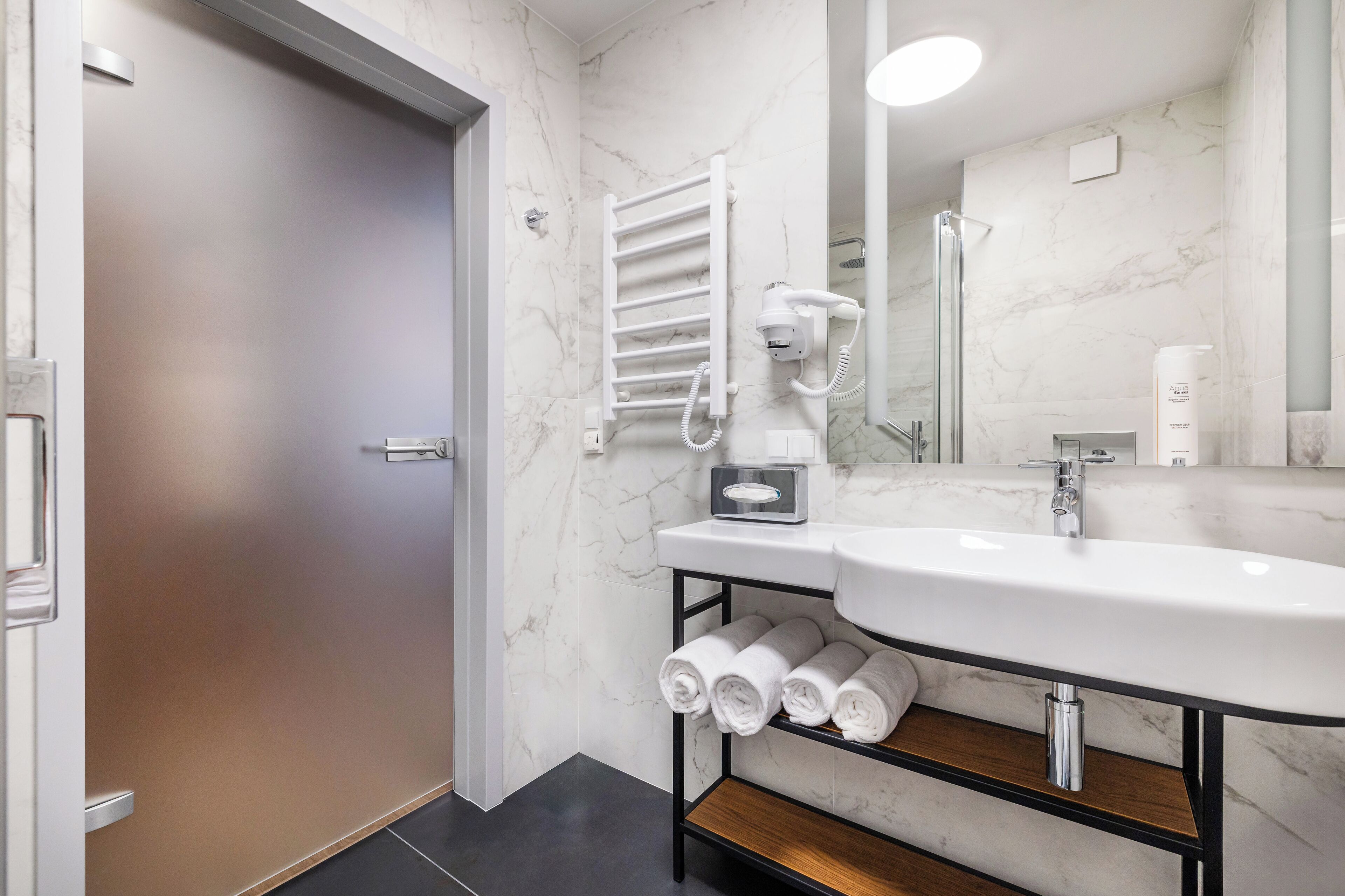 Un baño moderno con un lavamanos blanco, un perchero y un espejo.