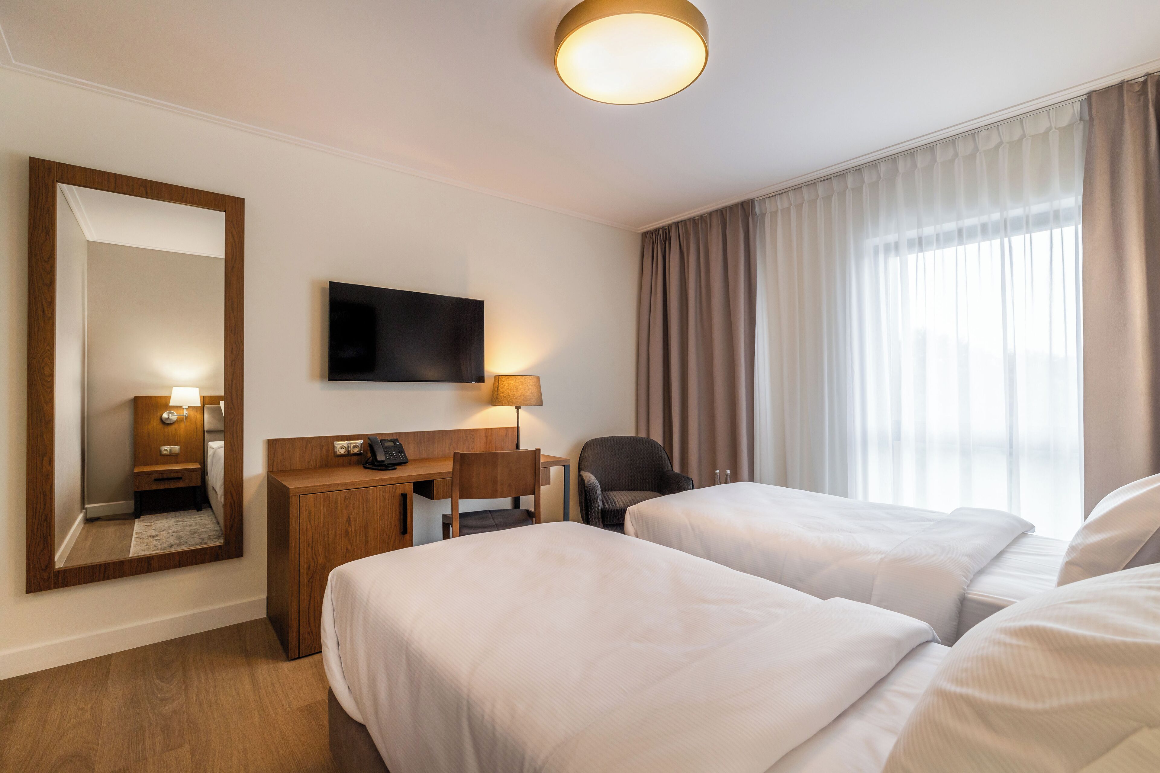Ein Hotelzimmer mit zwei Betten, einem Schreibtisch mit Stuhl, einem Fernseher und einem großen Spiegel.