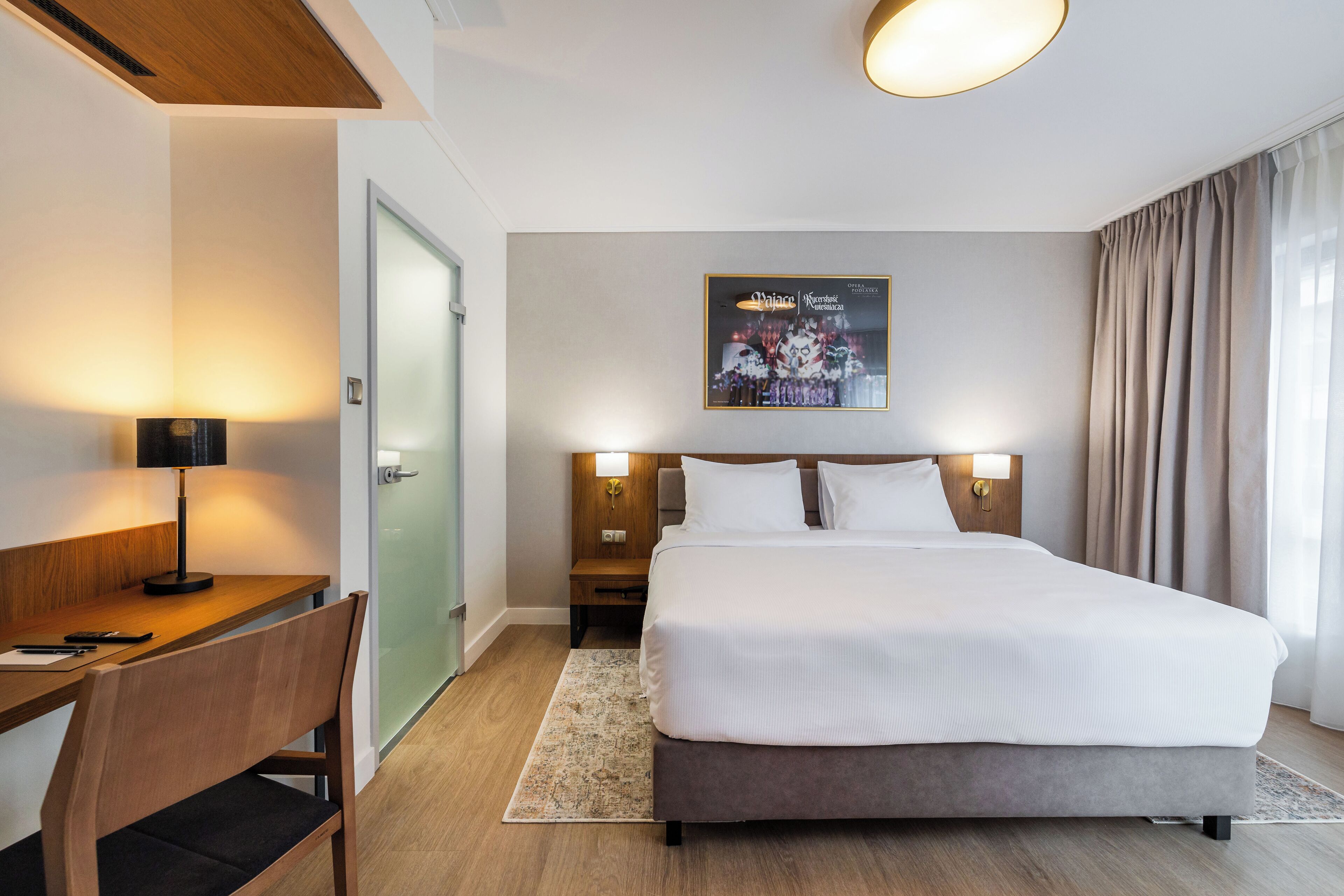 Una habitación de hotel con cama, escritorio, silla y un cartel en la pared.