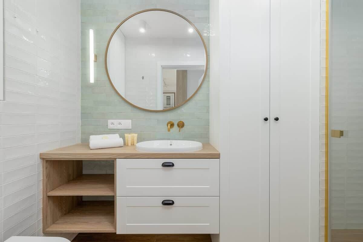 A bathroom with a white sink, wooden vanity, and a round mirror.