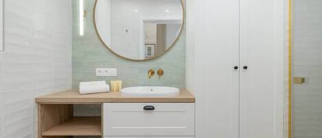 A bathroom with a white sink, wooden vanity, and a round mirror.
