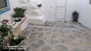 A stone-floored courtyard with a white door, potted plants, and a blue window frame. - CASAPANCHO 3 (CN)