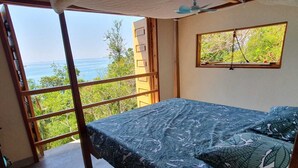 A bedroom with a bed, a window, and a view of the sea.