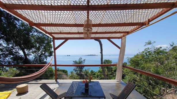 A covered outdoor seating area with a table and chairs, overlooking a scenic ocean view.